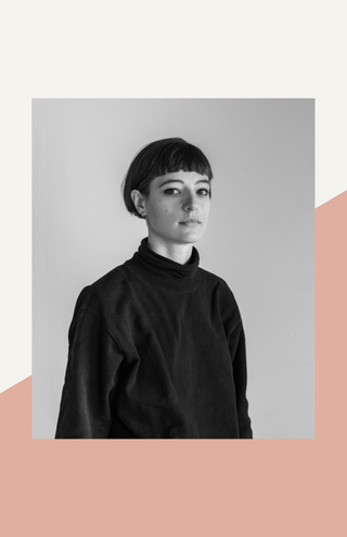 black and white image of a white woman with short dark hair standing at a quarter angle to camera. She is wearing a dark shirt with a high collar
